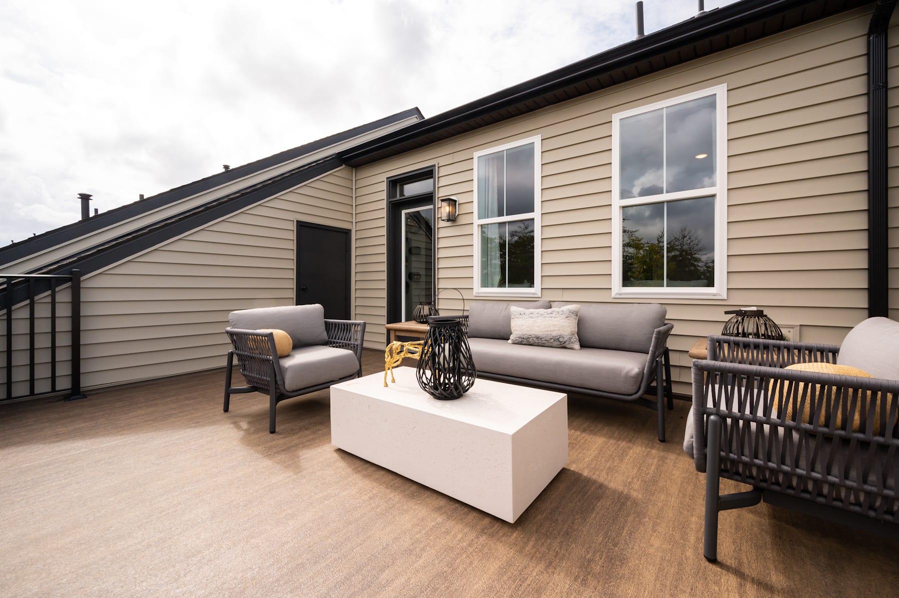 A cozy outdoor patio with comfortable seating, a coffee table, and a wooden exterior of the building in the background.