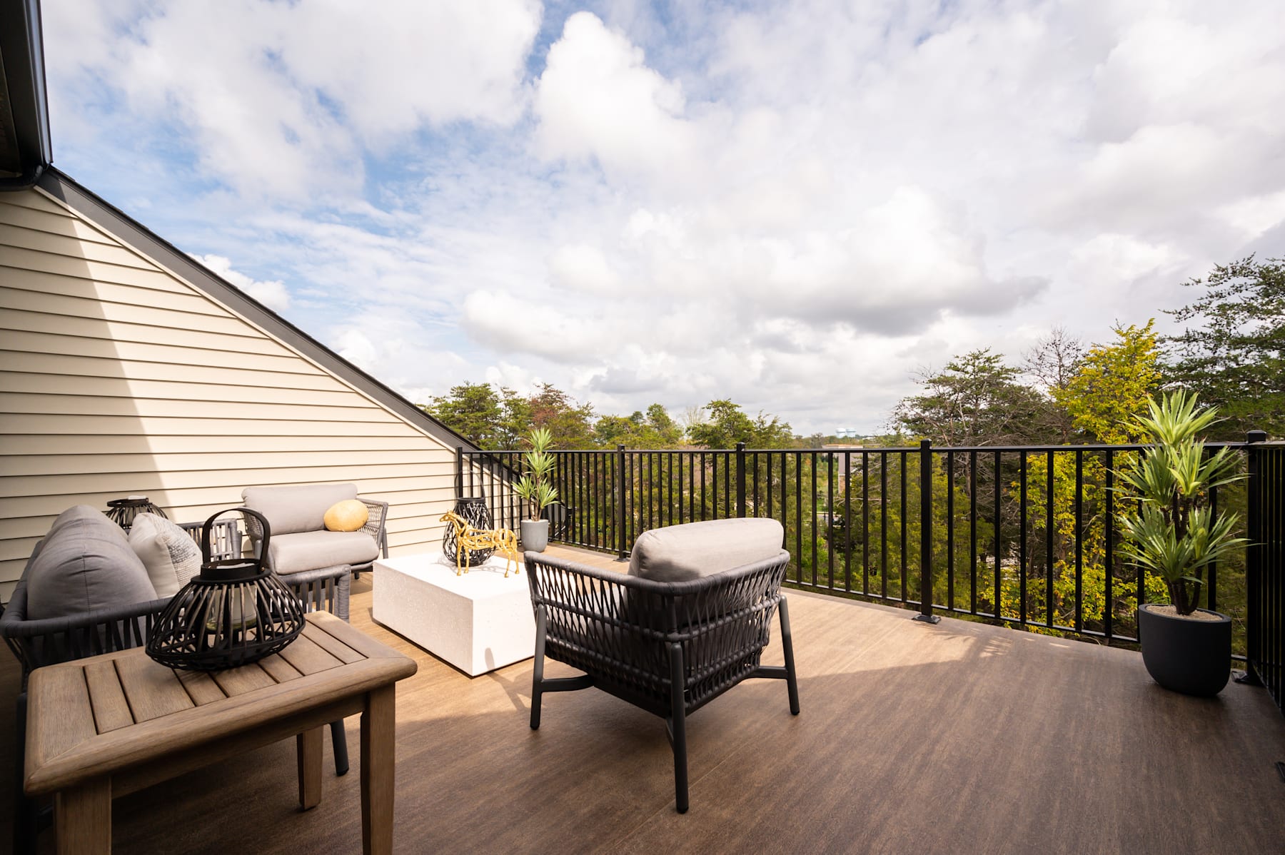 A cozy outdoor patio with wicker furniture, surrounded by lush greenery and a cloudy sky in the background.