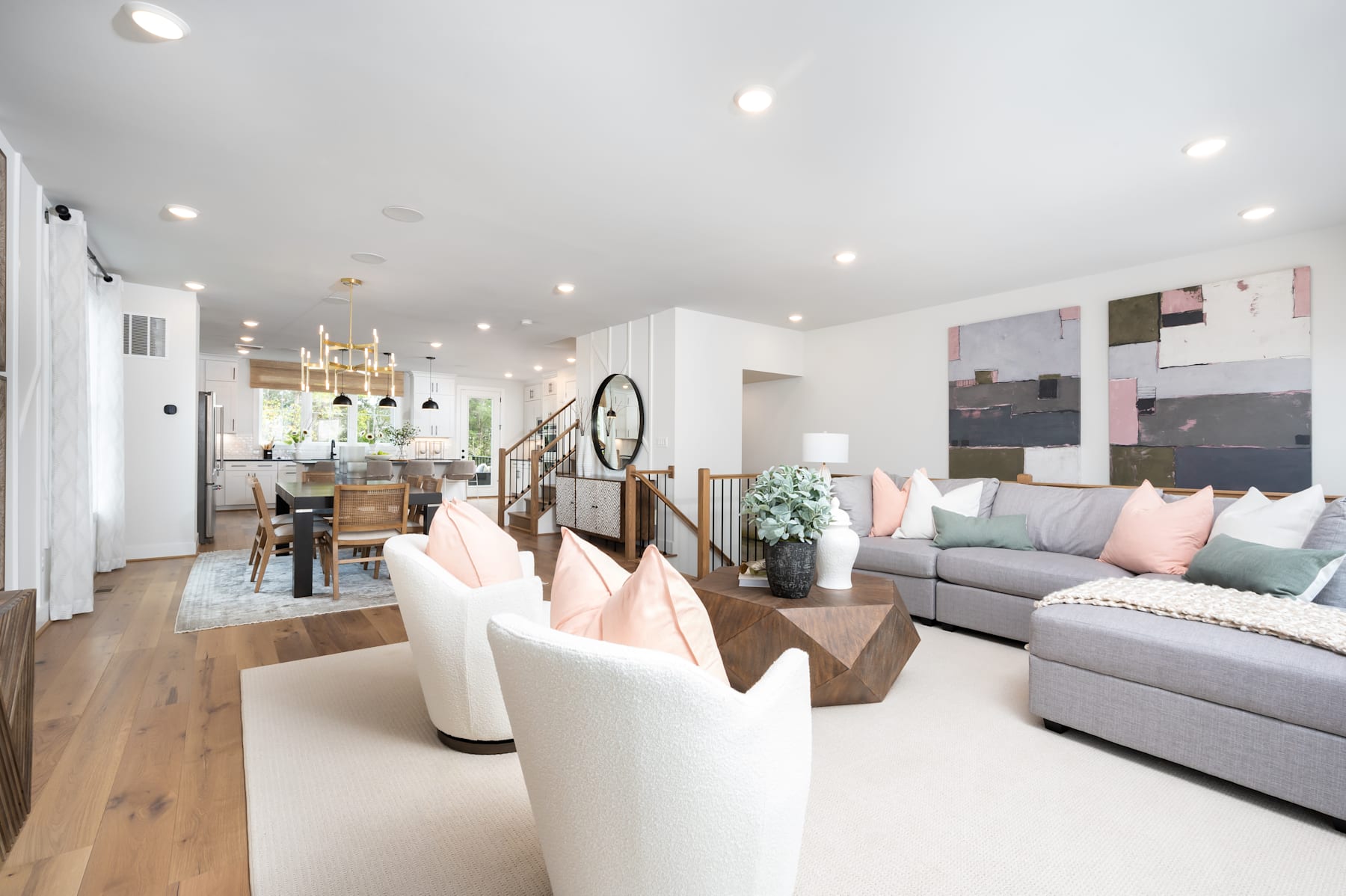 A spacious and well-designed living room with a cozy seating area, a dining table, and a kitchen visible in the background, all featuring a modern and minimalist aesthetic with a mix of neutral and pastel colors.