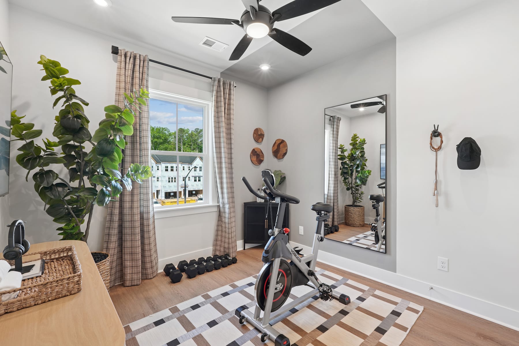 A well-furnished home gym with a ceiling fan, potted plants, and various exercise equipment, including a stationary bike, set against a bright and airy backdrop.