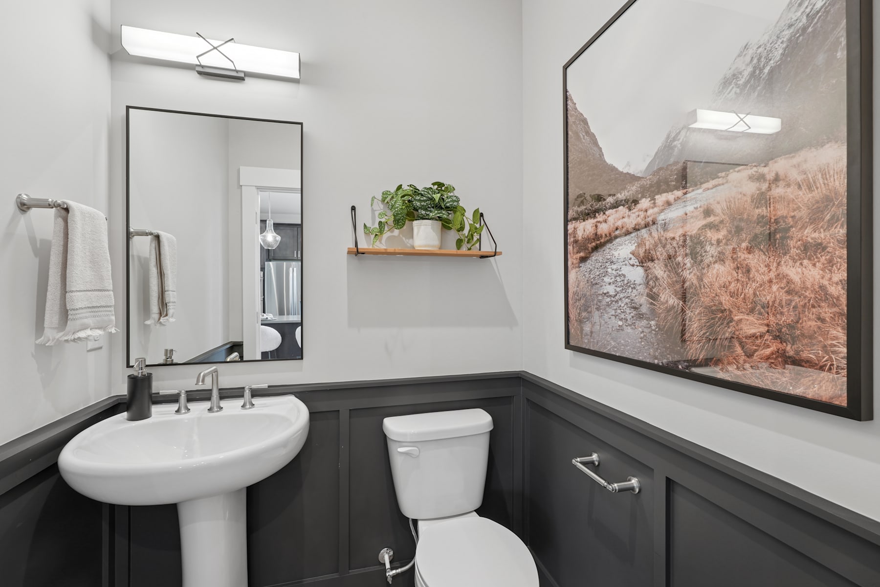 A modern bathroom with a white pedestal sink, a toilet, and a large framed landscape photograph on the wall, creating a serene and minimalist atmosphere.