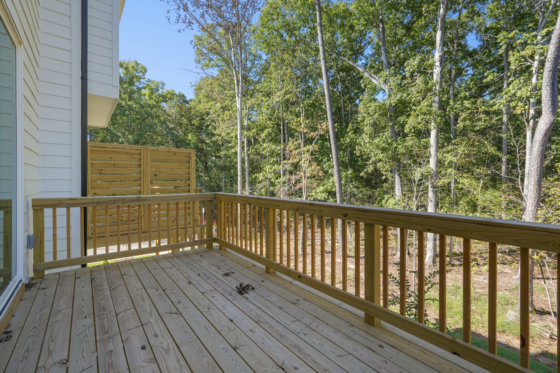 A wooden deck with a railing overlooks a lush, forested area with tall trees and greenery in the background.
