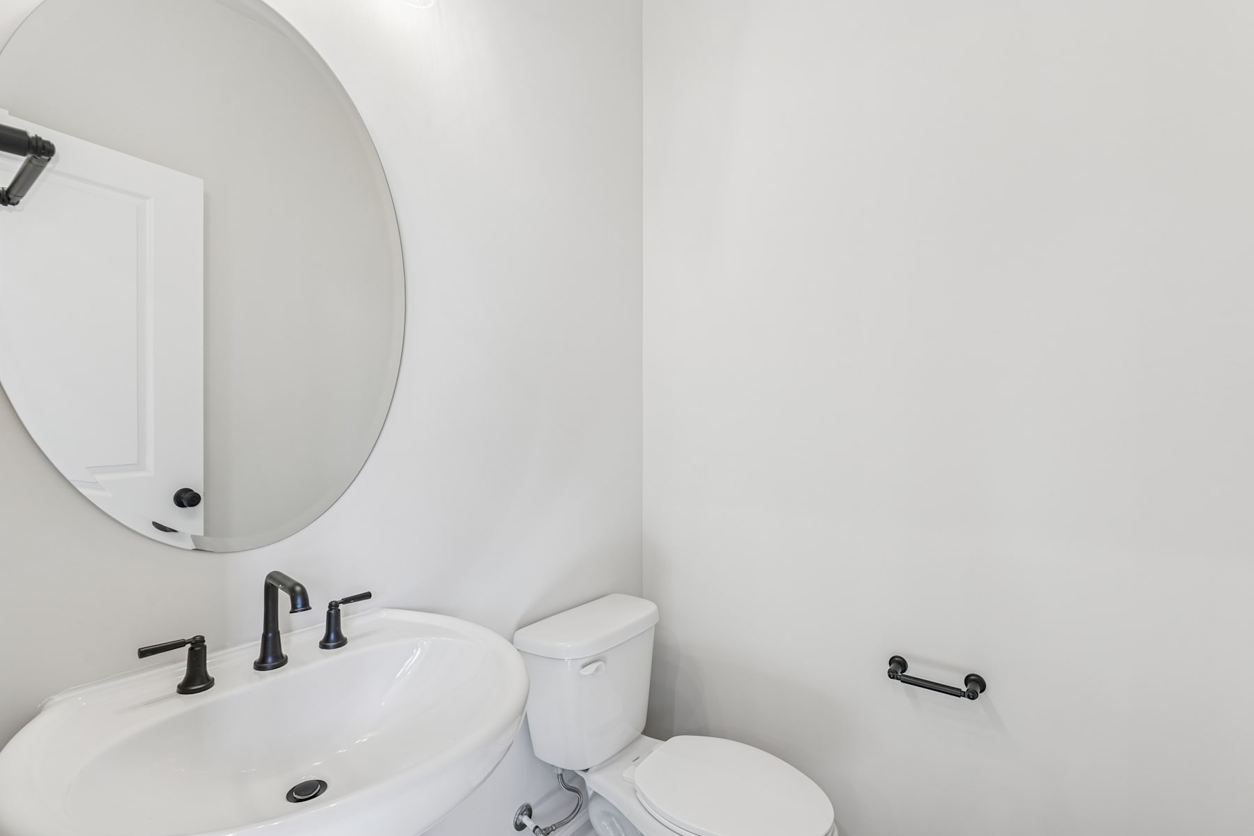 A modern, minimalist bathroom with a round mirror, a white sink, and a toilet visible.