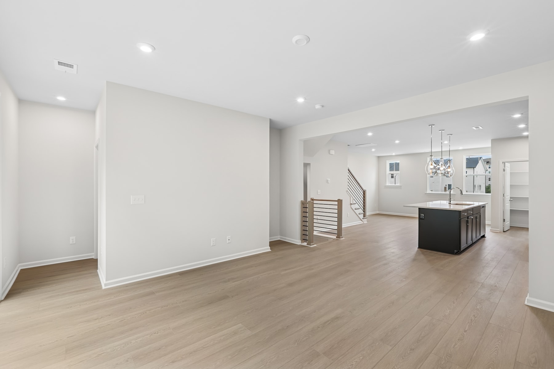 A spacious, modern interior with white walls, hardwood floors, and a kitchen island in the background.