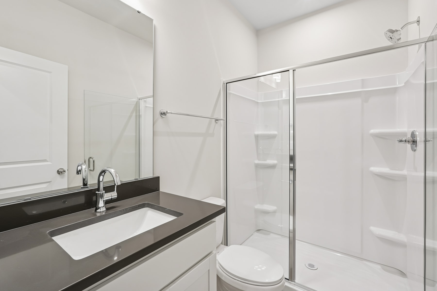 A modern, minimalist bathroom with a white sink, dark countertop, and a glass-enclosed shower stall.