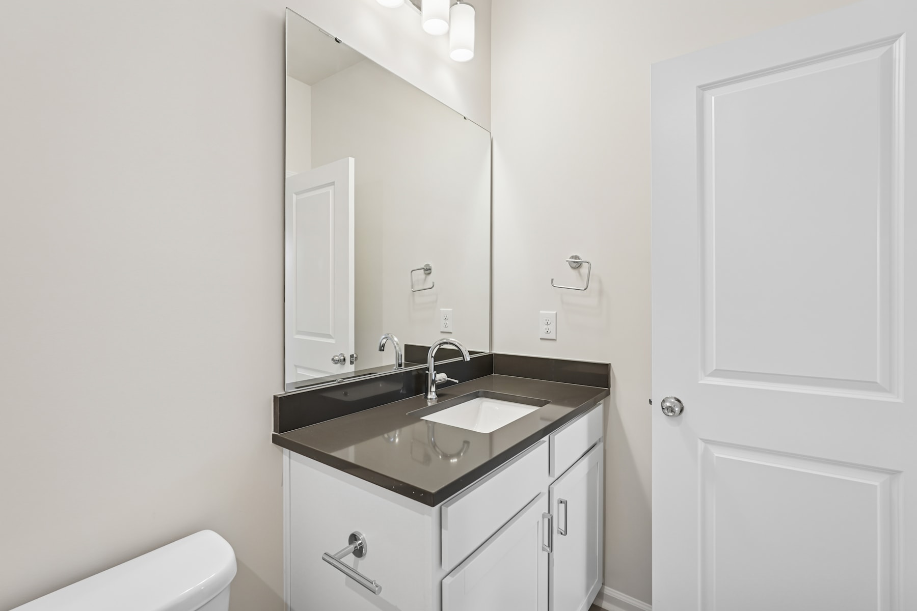 A modern, minimalist bathroom with a white vanity, black countertop, and a large mirror on the wall.