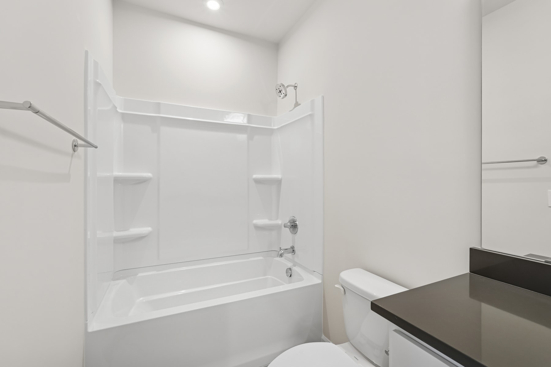 A modern, minimalist bathroom with a white tiled shower enclosure, a vanity with a dark countertop, and a toilet in the background.