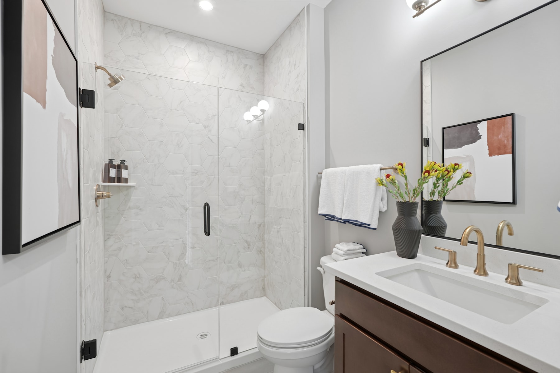 A modern and minimalist bathroom with a white marble-like tile wall, a vanity with a white countertop, and a framed artwork on the wall.