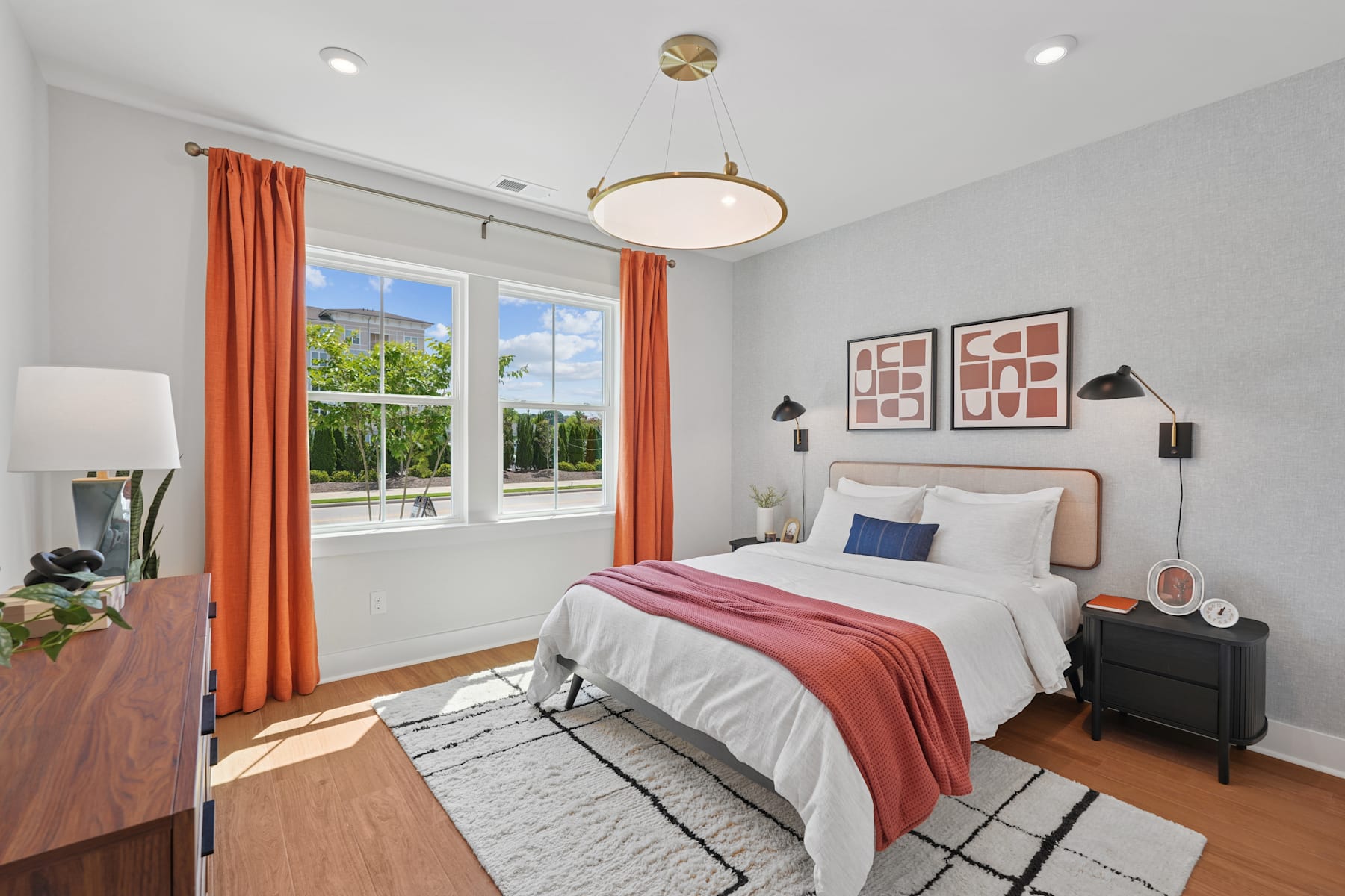 A cozy and well-decorated bedroom with a large window, a plush bed, and vibrant curtains, set against a backdrop of lush greenery outside.