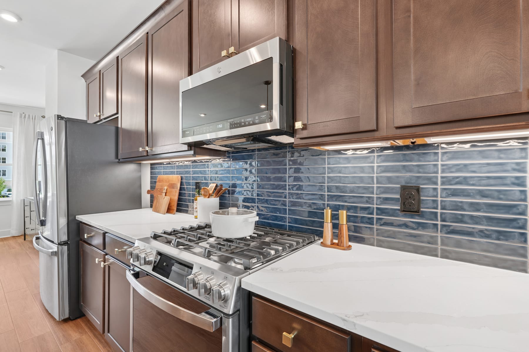 A modern kitchen with dark wood cabinets, a gas stove, and a tiled backsplash in shades of blue.
