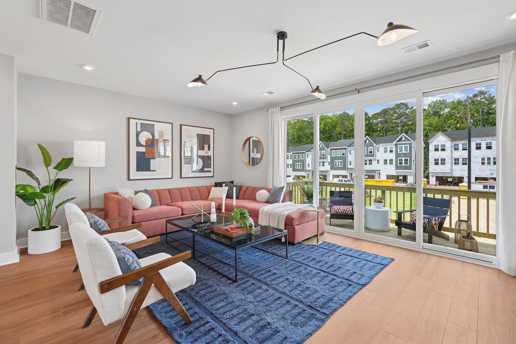 A modern and cozy living room with a pink sofa, a blue patterned rug, and large windows overlooking a residential neighborhood.