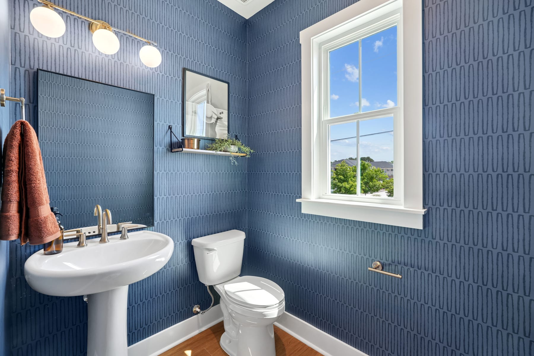 A modern bathroom with blue tiled walls, a white pedestal sink, and a window overlooking a scenic outdoor view.