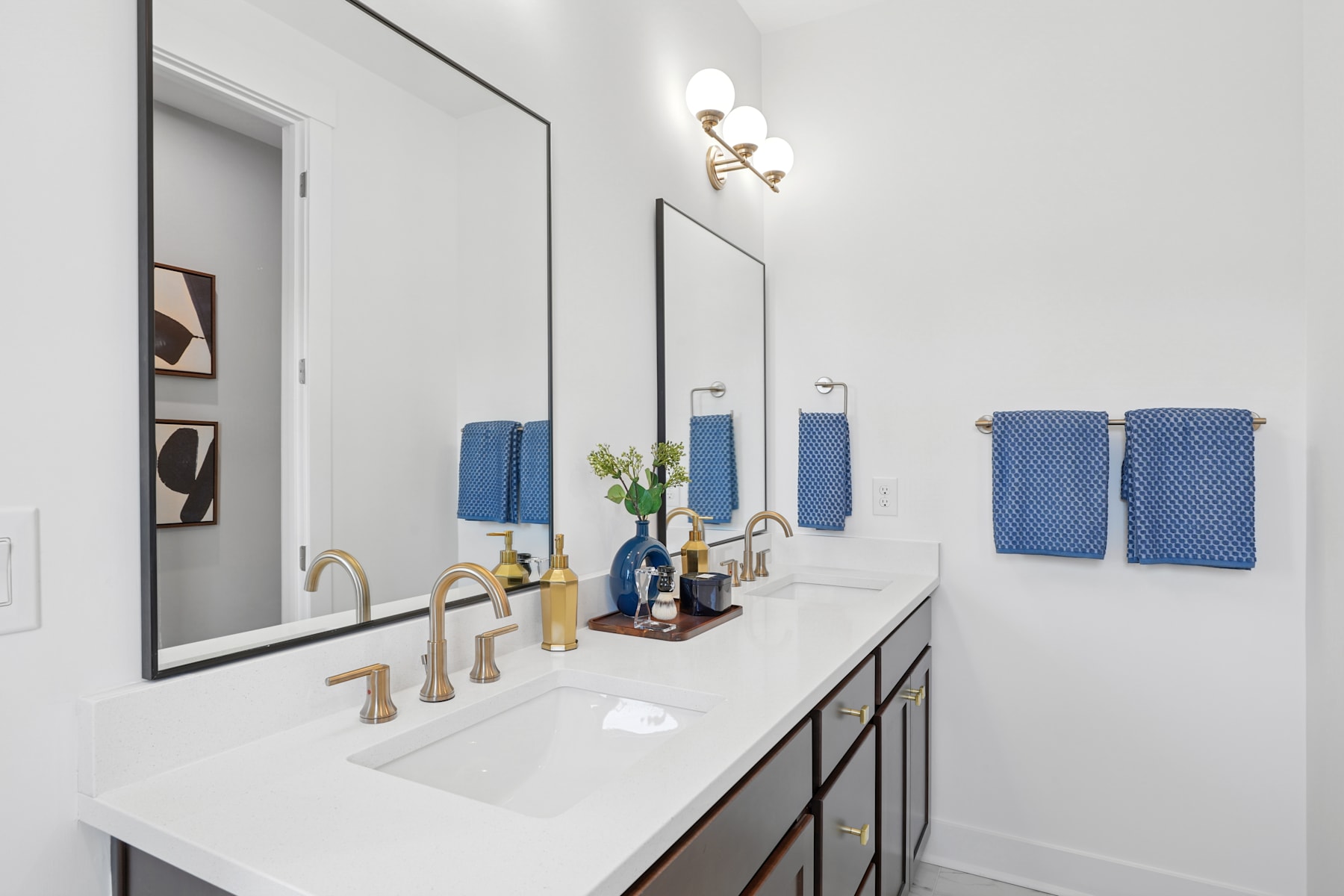 A modern and well-designed bathroom with a double vanity, large mirrors, and decorative accents such as towels and a vase.