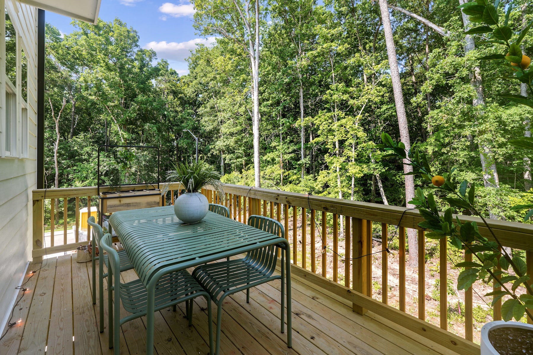 A wooden deck with a patio set overlooking a lush, green forest landscape on a sunny day.