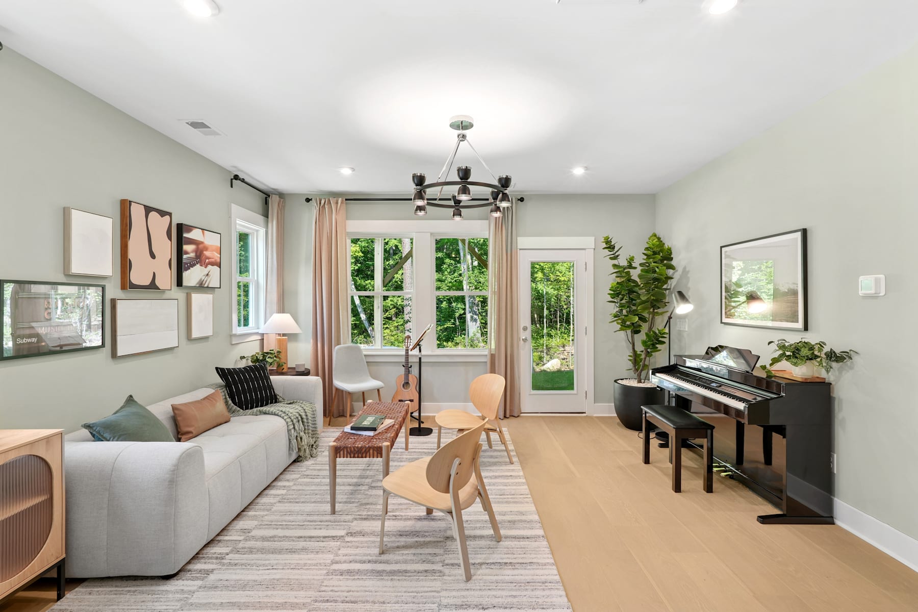 A cozy and well-furnished living room with a gray sofa, wooden chairs, a piano, and various decorative elements, surrounded by large windows overlooking a lush outdoor environment.