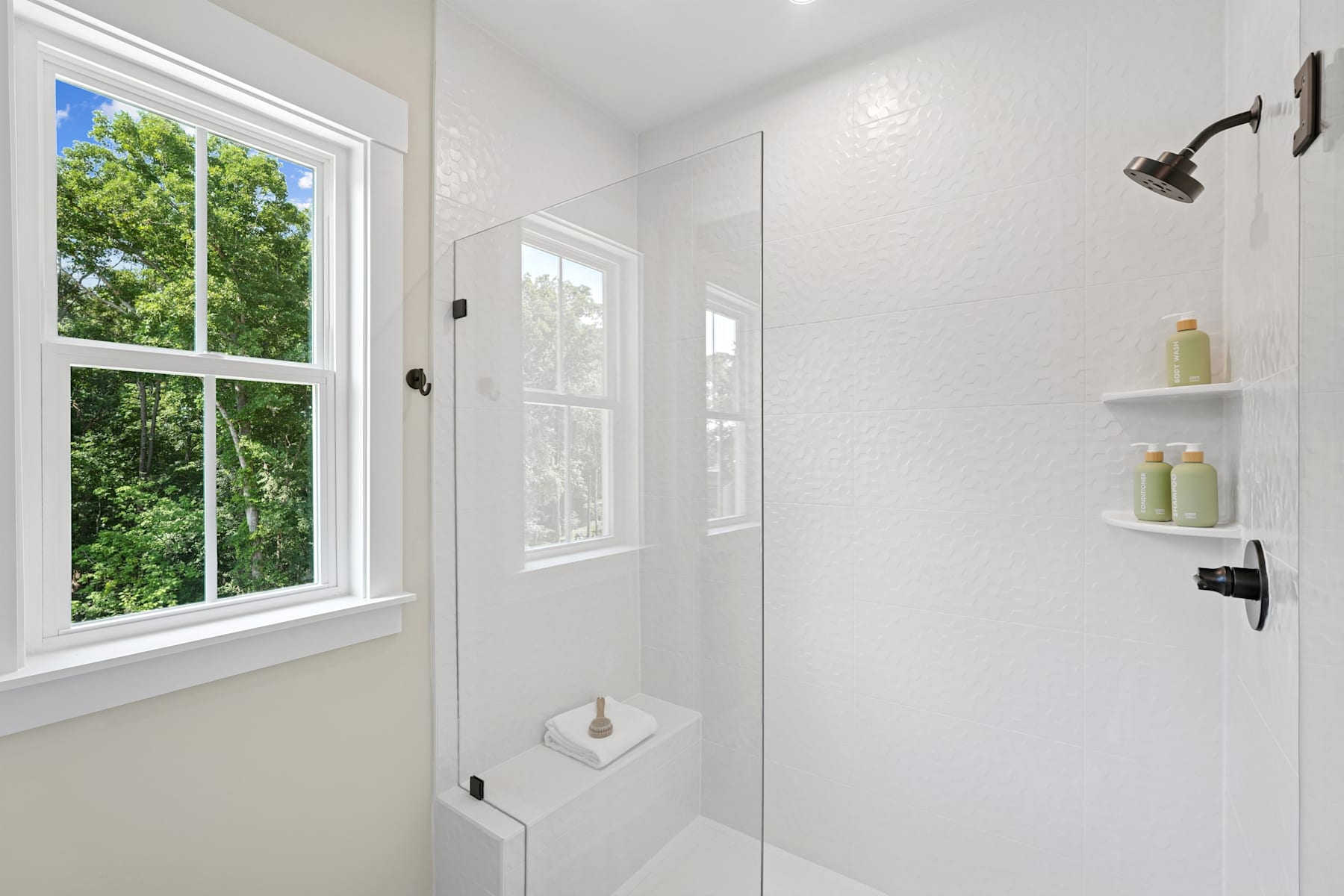 A bright and airy bathroom with a large window overlooking lush greenery, featuring a minimalist design with white walls, a glass shower enclosure, and shelving for toiletries.