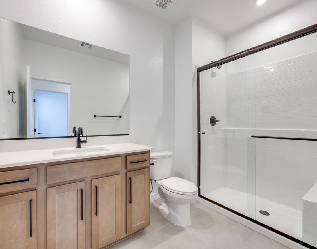 A modern and minimalist bathroom with a wooden vanity, a large mirror, and a glass shower enclosure.