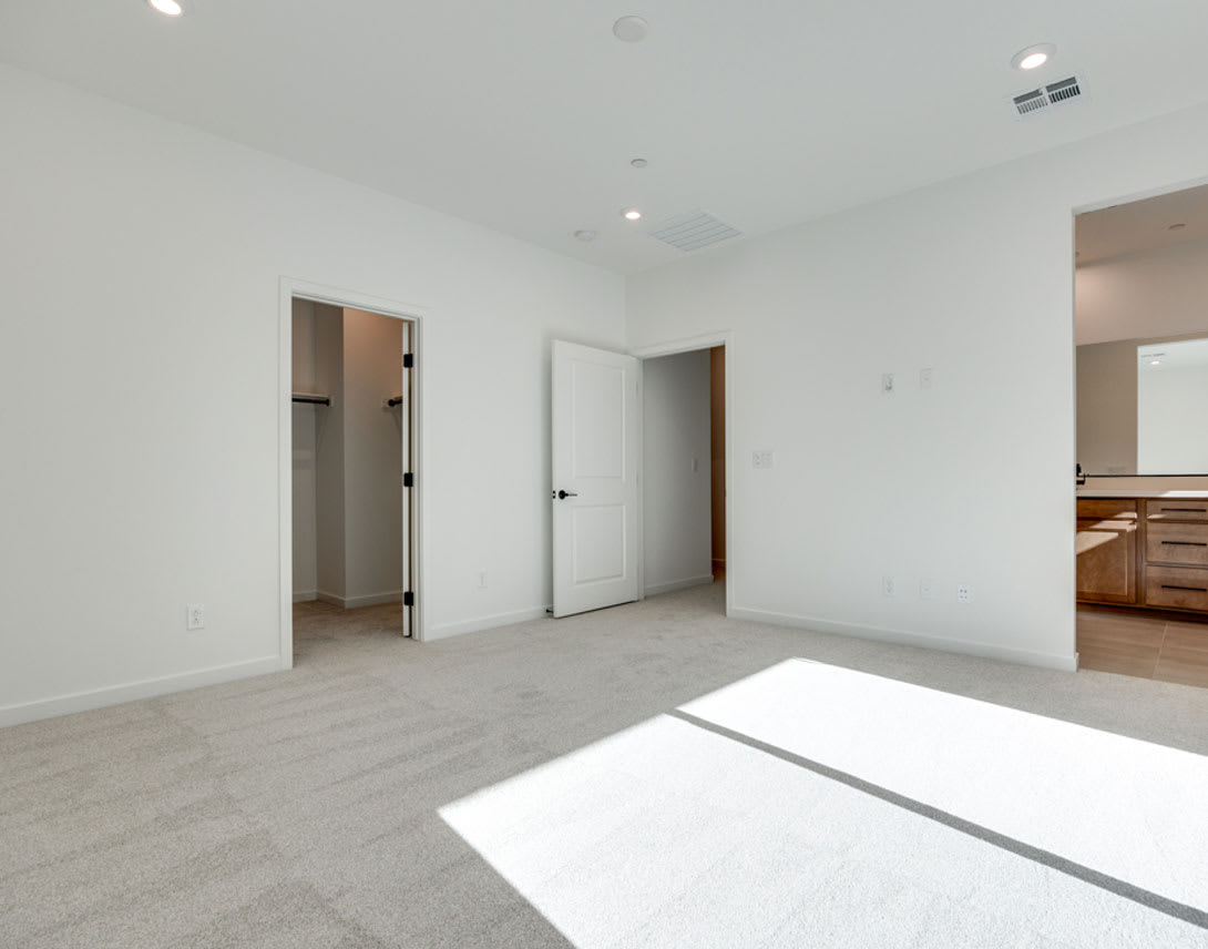 A spacious, minimalist room with white walls, gray flooring, and a doorway leading to another area.