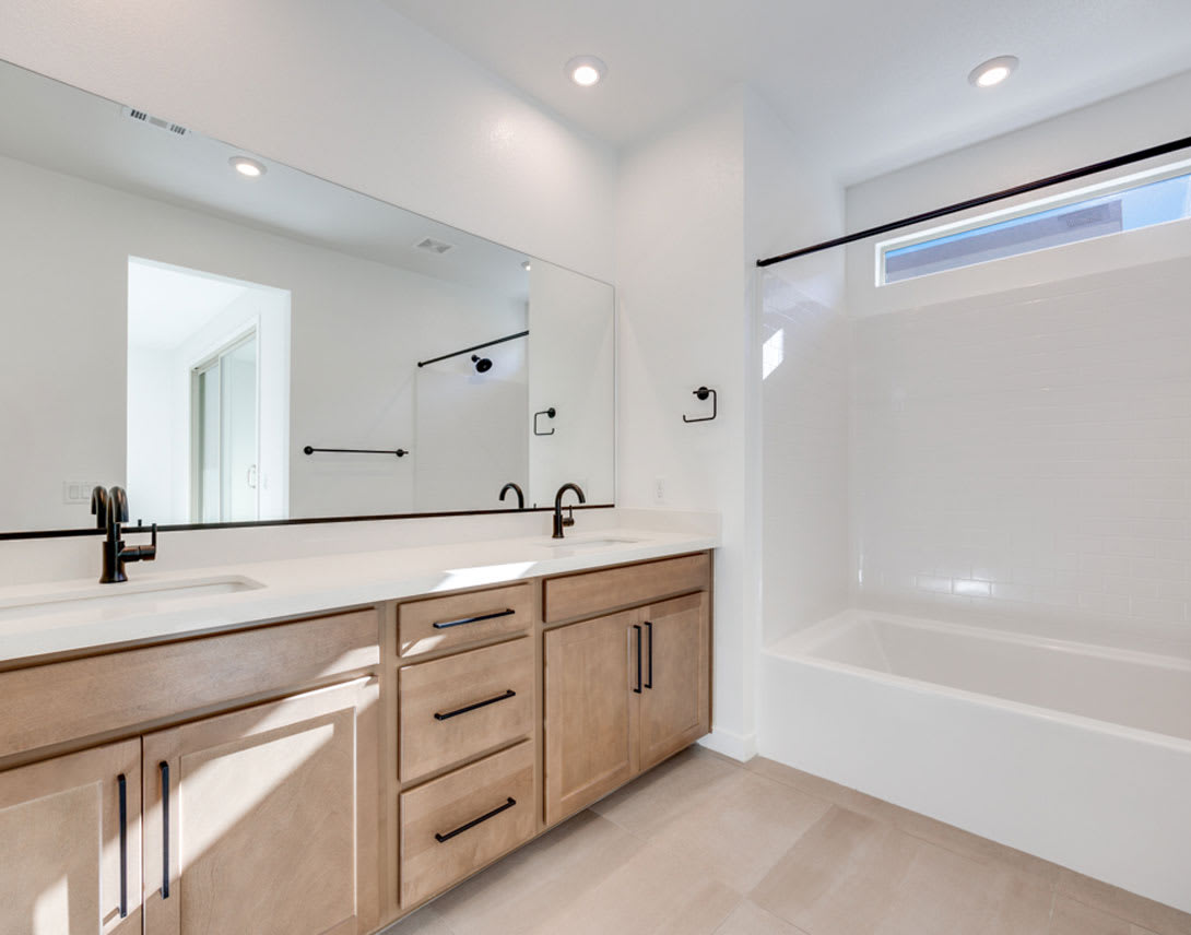 A modern and minimalist bathroom with a wooden vanity, black fixtures, and a large mirror, set against a bright and airy background.