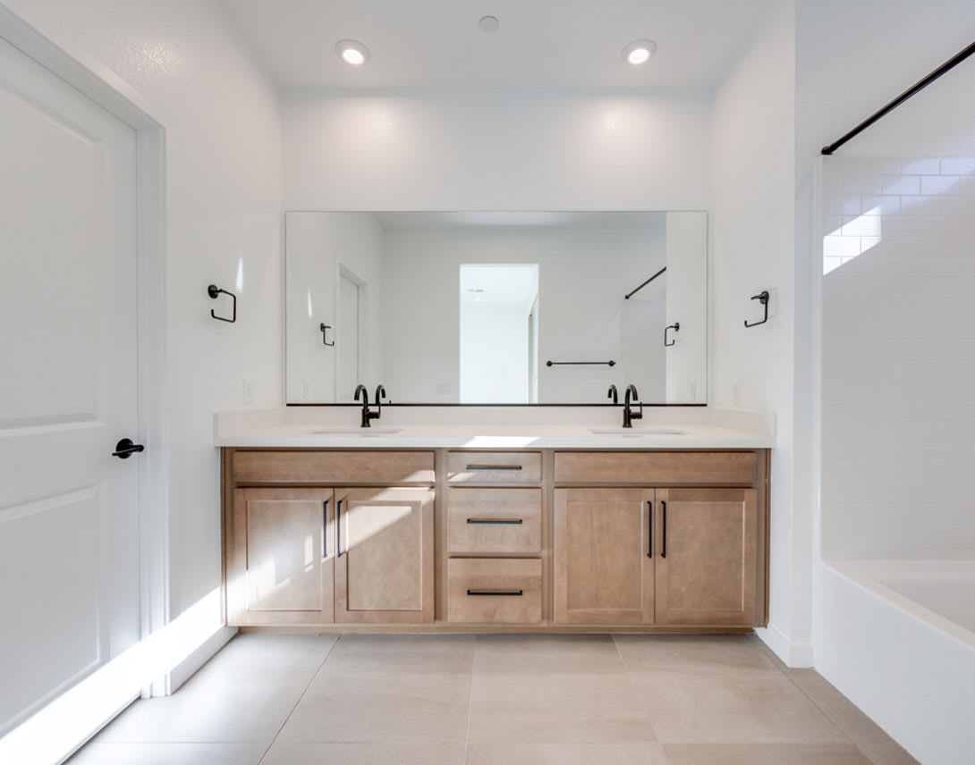 A modern and minimalist bathroom vanity with a large mirror, wooden cabinets, and black fixtures, set against a bright and airy background.