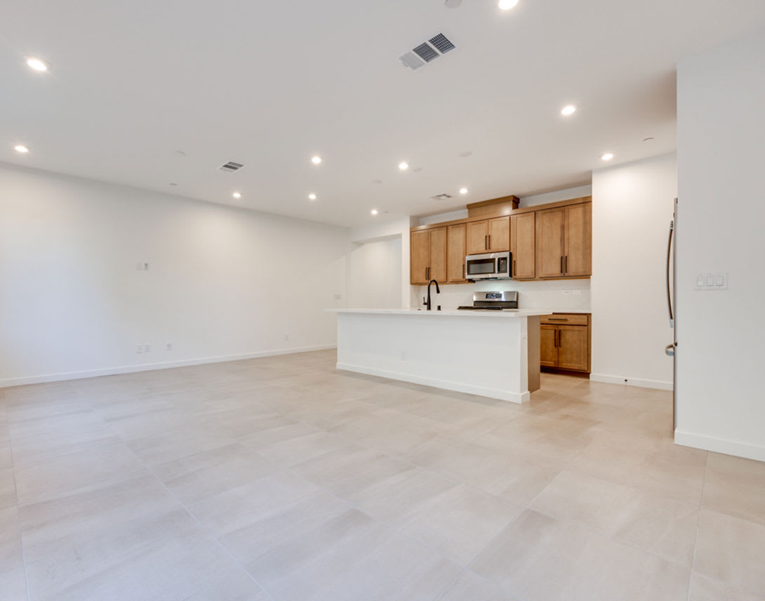 A spacious, open-concept kitchen and living area with light-colored wood cabinets, a white countertop, and a stainless steel appliance visible in the background.