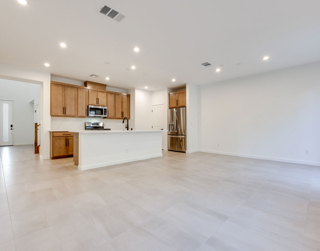 A spacious, open-concept kitchen and living area with light-colored wood cabinets, stainless steel appliances, and a bright, airy atmosphere.