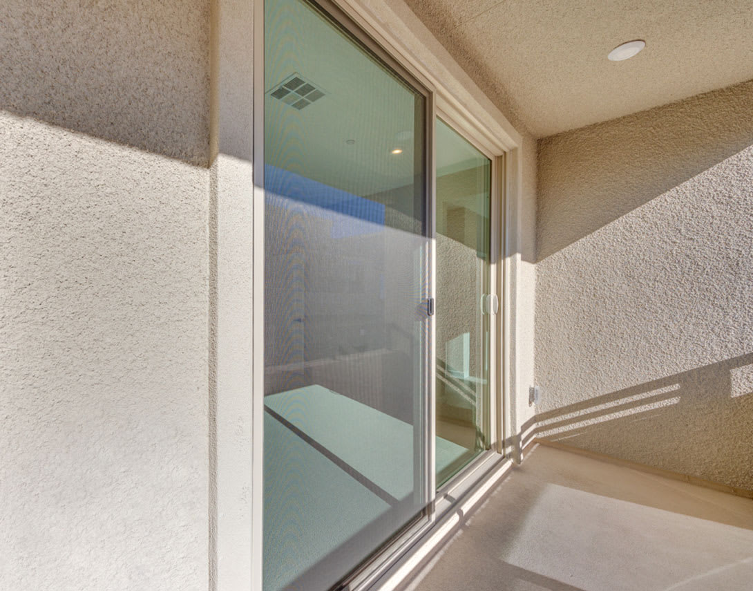 A glass door leading to a balcony or patio, with a beige wall and a recessed lighting fixture visible in the background.