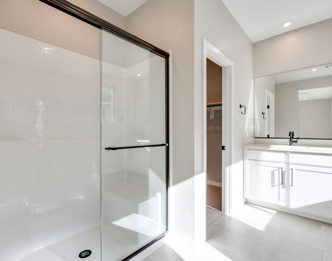 A modern, minimalist bathroom with a glass shower enclosure, white walls, and a vanity with a sink visible in the background.