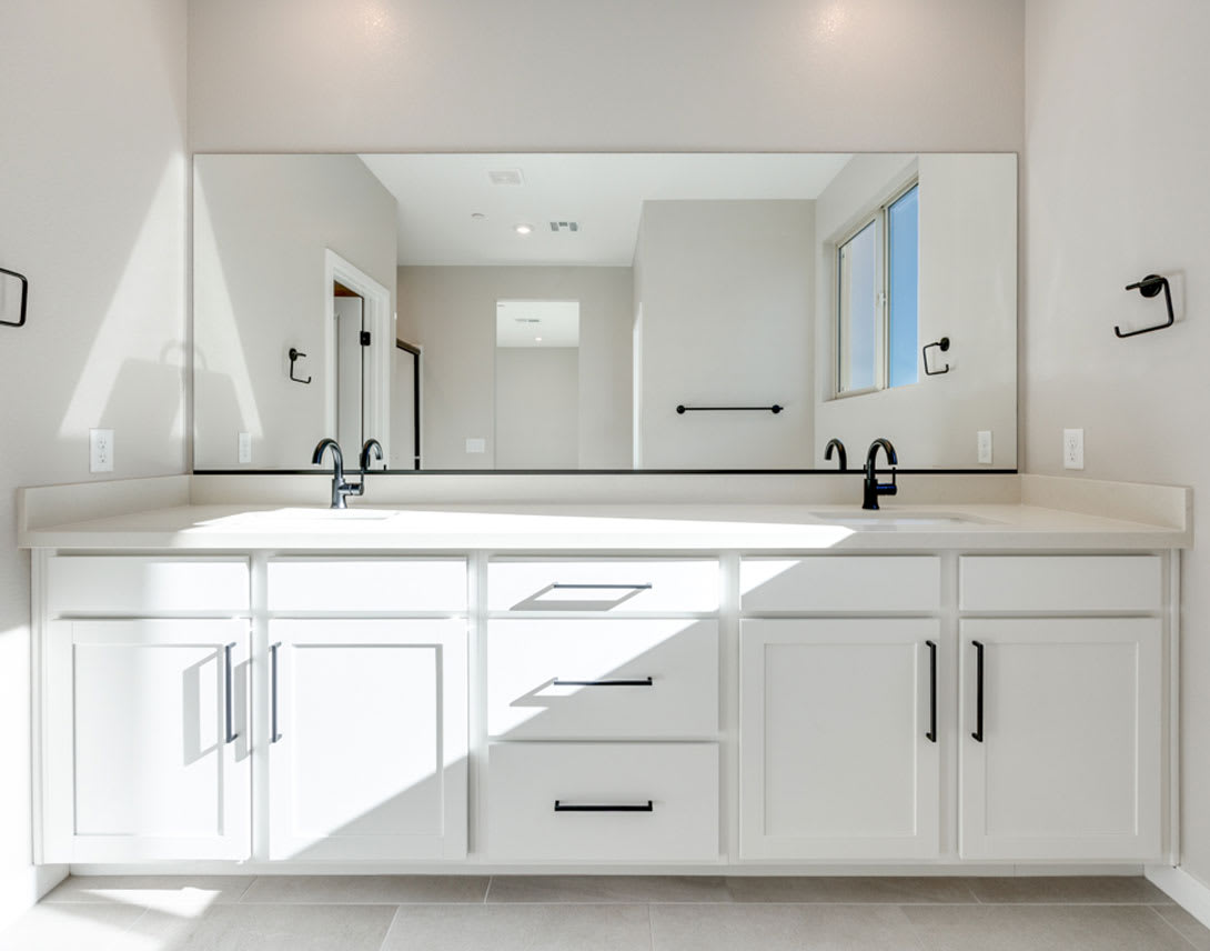 A modern, minimalist bathroom with a large vanity, double sinks, and a large mirror taking up the majority of the wall space.