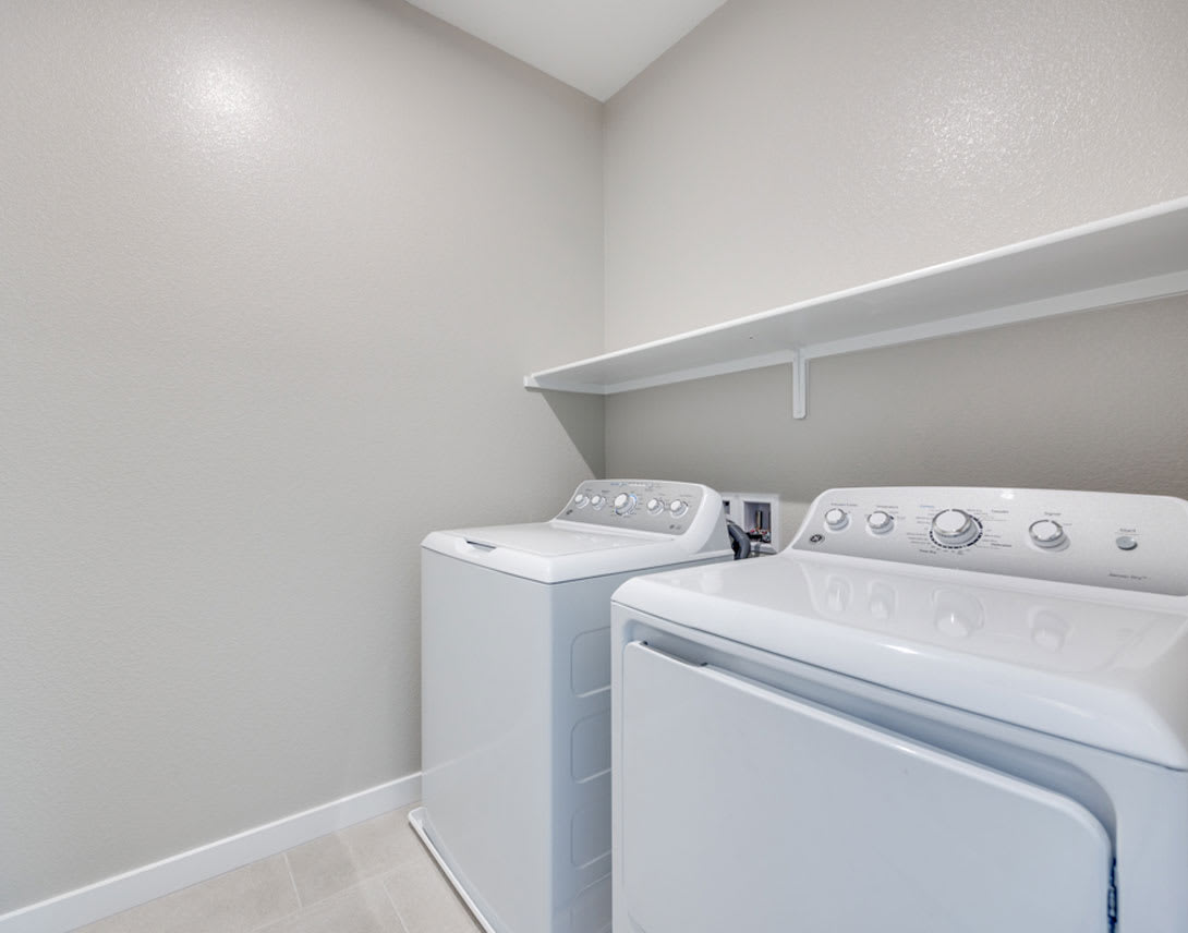 A bright, modern laundry room with a washing machine and dryer set against a plain white wall.