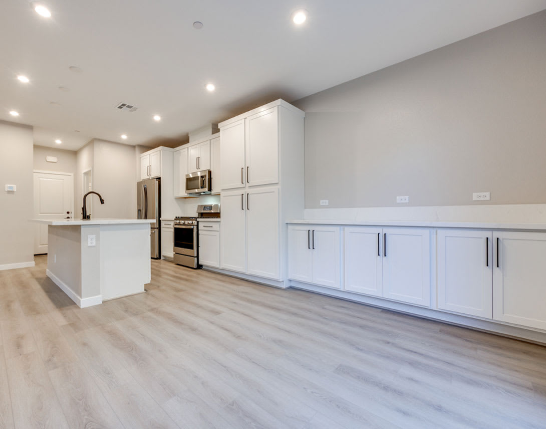A modern, open-concept kitchen with white cabinets, stainless steel appliances, and a hardwood floor that extends throughout the space.