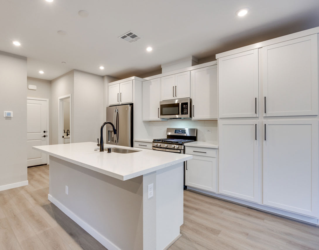 A modern, well-lit kitchen with white cabinets, stainless steel appliances, and a central island with a white countertop.