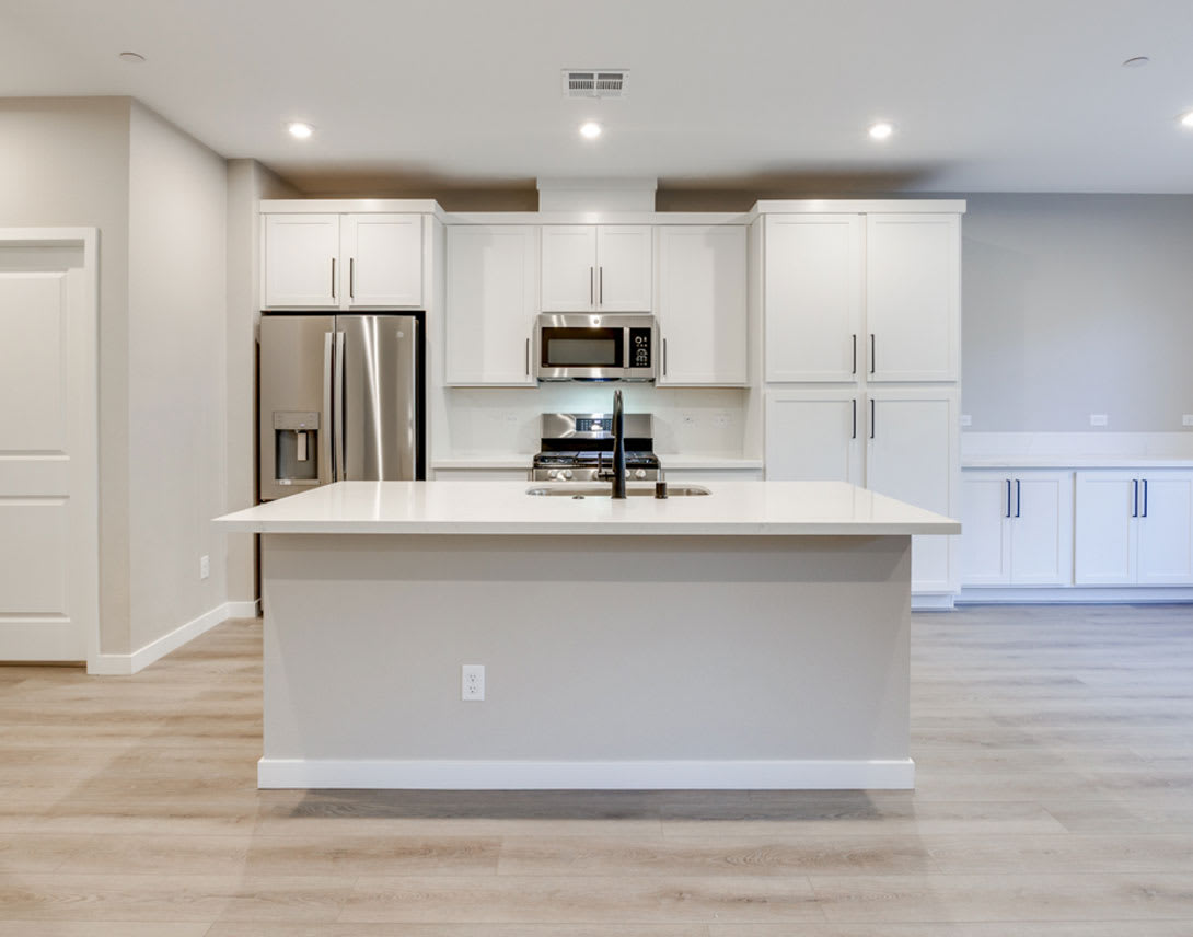A modern, open-concept kitchen with white cabinets, stainless steel appliances, and a large central island with a countertop.