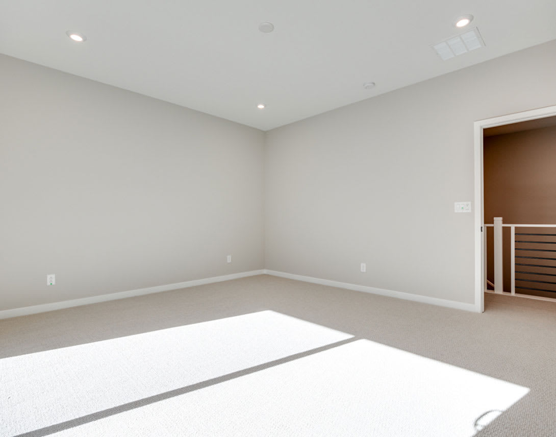 An empty, well-lit room with white walls and a wooden door visible in the background.