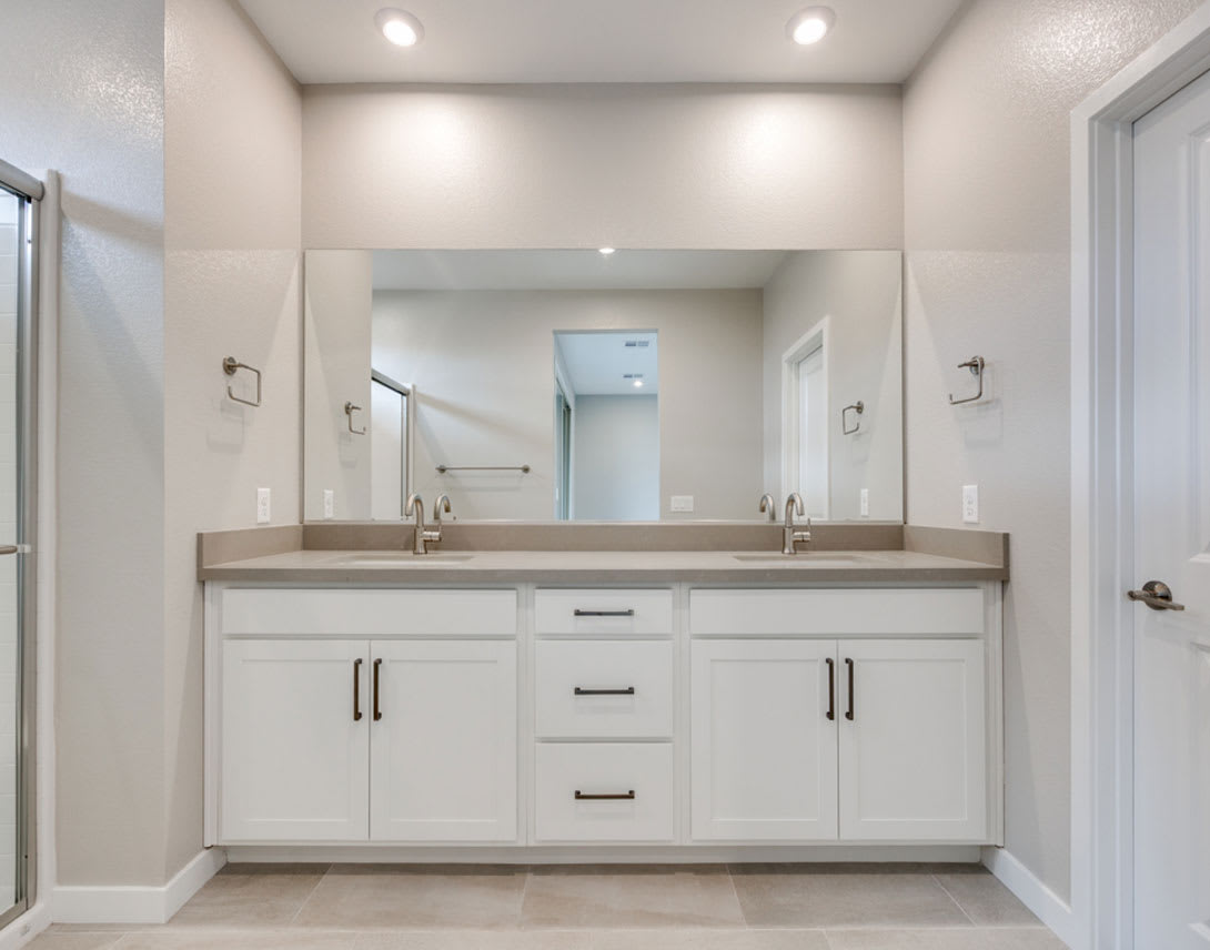 A spacious and well-lit bathroom with a double vanity, white cabinets, and a large mirror taking up the majority of the wall space.