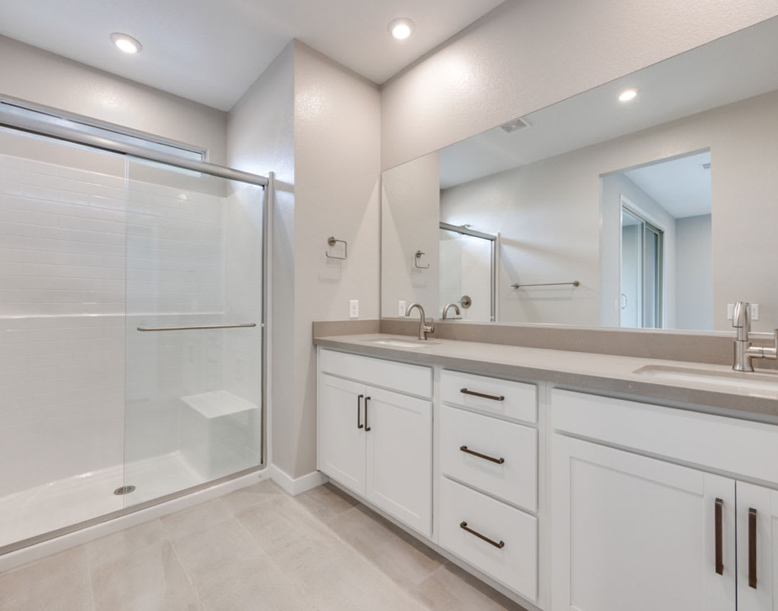 A modern, well-lit bathroom with a large vanity, a walk-in shower, and recessed lighting fixtures on the ceiling.