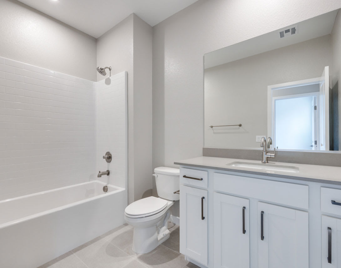 A modern, well-lit bathroom with a white vanity, toilet, and bathtub surrounded by neutral-colored walls and fixtures.