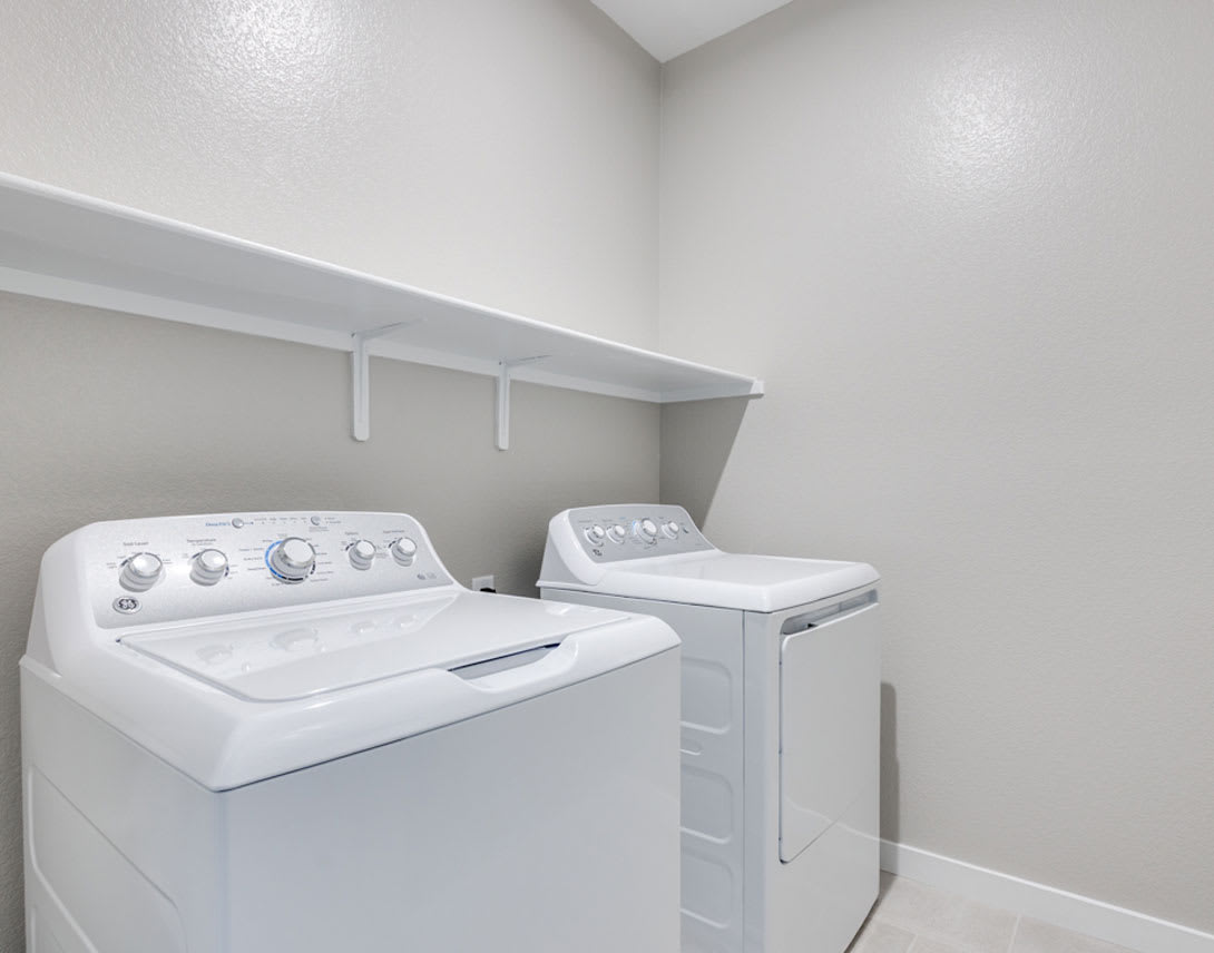 A small laundry room with a white washing machine and dryer, shelves above, and a neutral-colored wall background.