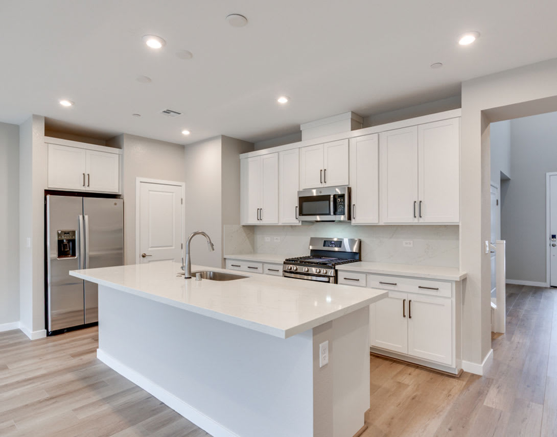 A modern, open-concept kitchen with white cabinets, stainless steel appliances, and a large central island with a white countertop.