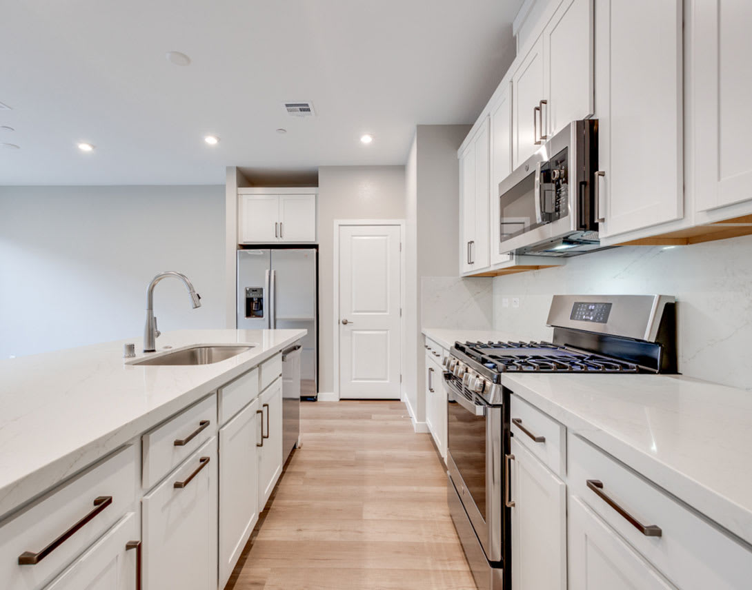 A modern, well-equipped kitchen with white cabinets, stainless steel appliances, and a hardwood floor.