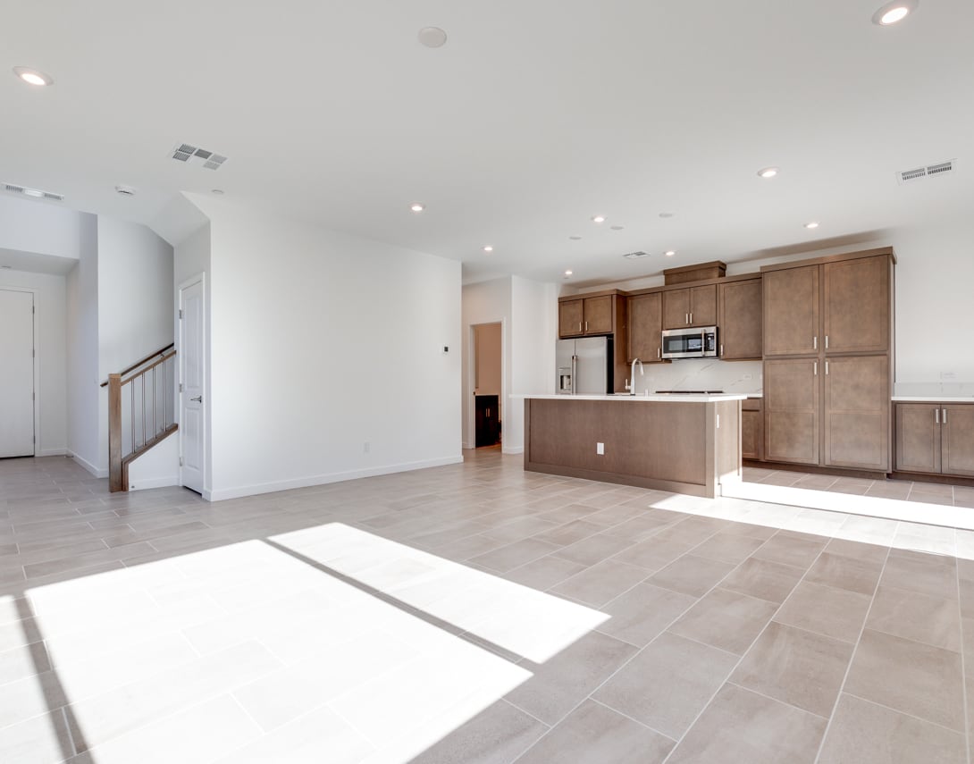 A spacious and modern open-plan kitchen and living area with light-colored wood cabinets, stainless steel appliances, and a tiled floor.