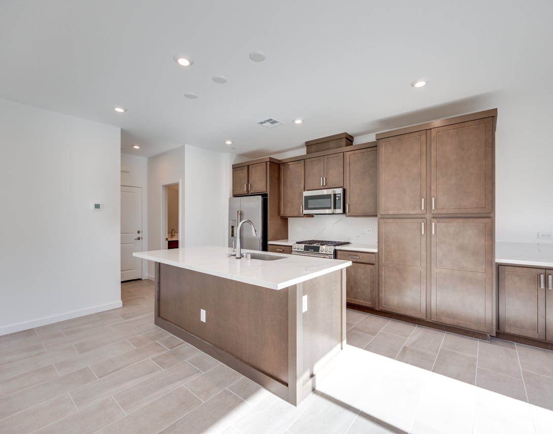 A modern, open-concept kitchen with light-colored wood cabinets, a large island, and stainless steel appliances, set against a bright, airy background.