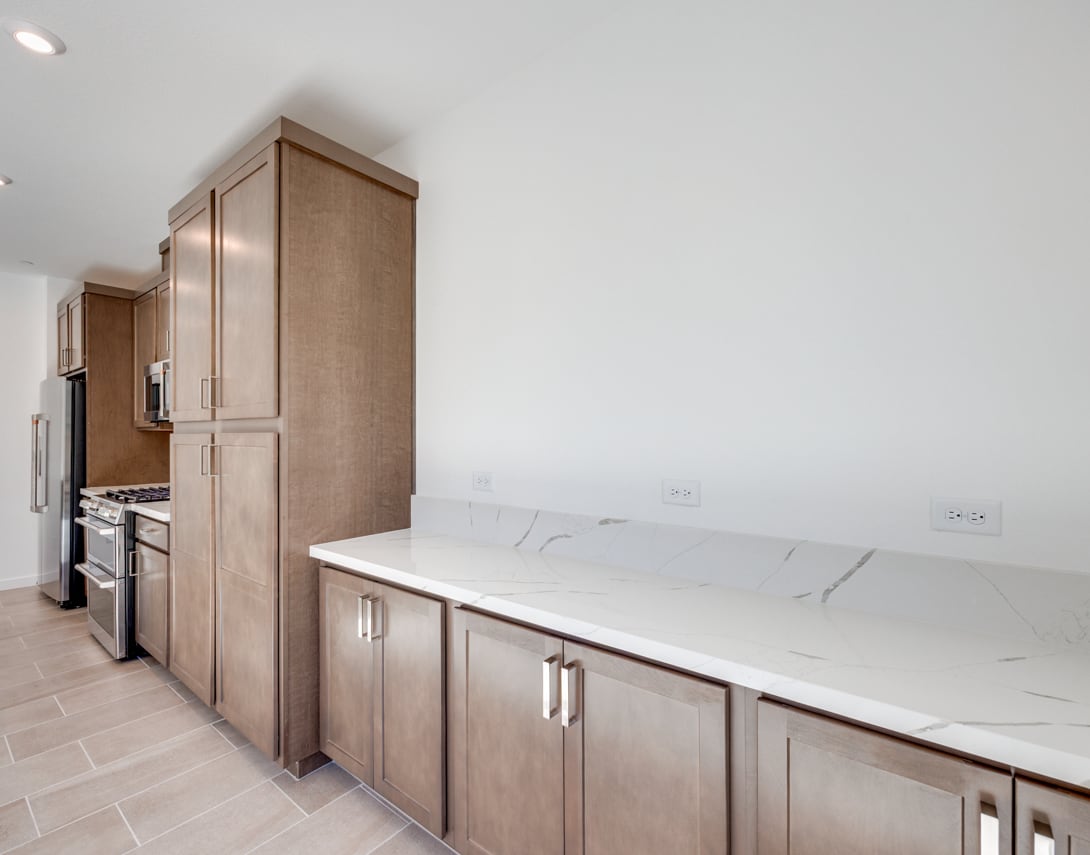 A modern kitchen with wooden cabinets, a marble countertop, and stainless steel appliances.