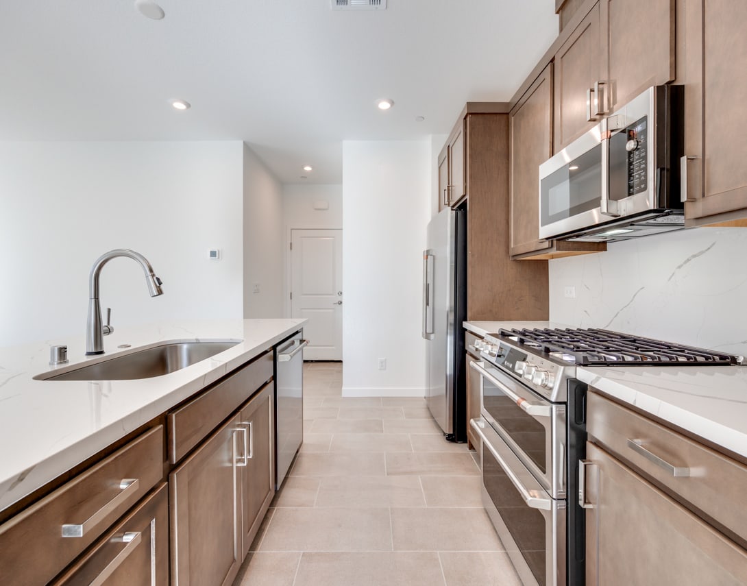 A modern, well-equipped kitchen with wooden cabinets, stainless steel appliances, and a tiled floor.