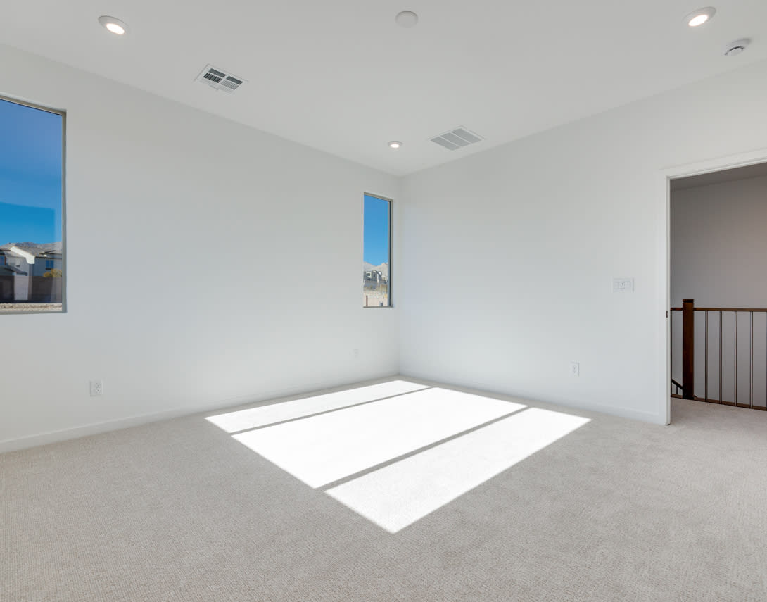 A spacious, well-lit room with white walls, a carpeted floor, and a window providing natural light.
