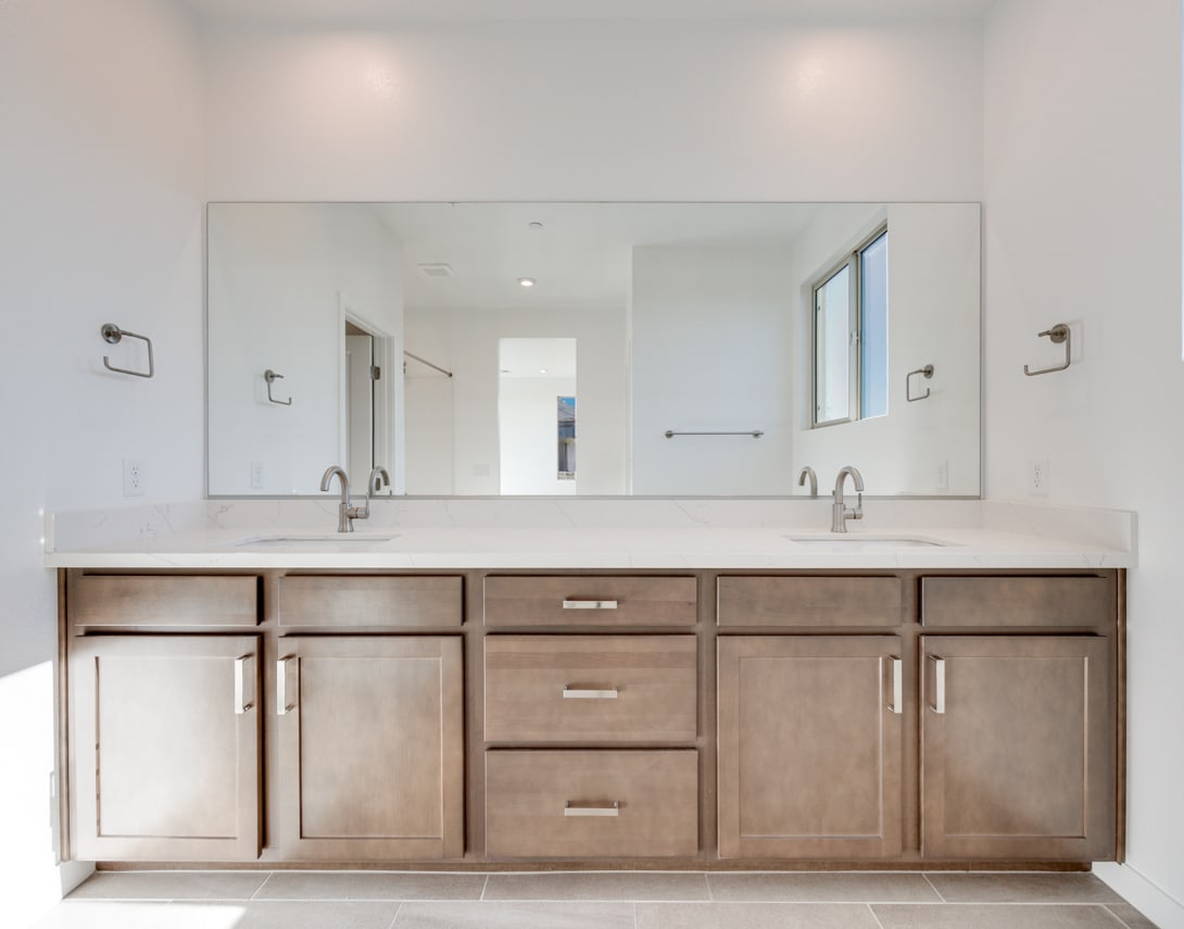 A modern and spacious bathroom with a large vanity cabinet, double sinks, and a large mirror taking up the entire wall.
