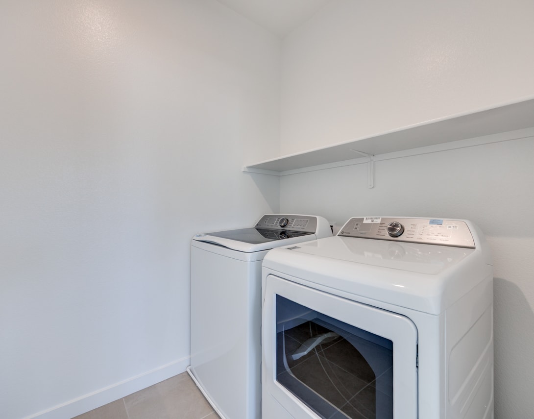 A white washing machine and dryer are placed in a small, bright room with white walls.