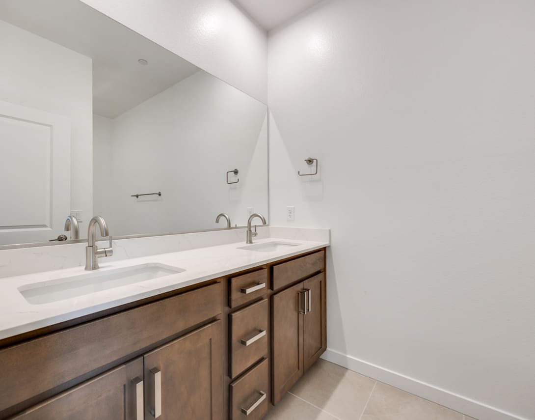 A modern bathroom vanity with a white countertop and wooden drawers, set against a plain white wall background.