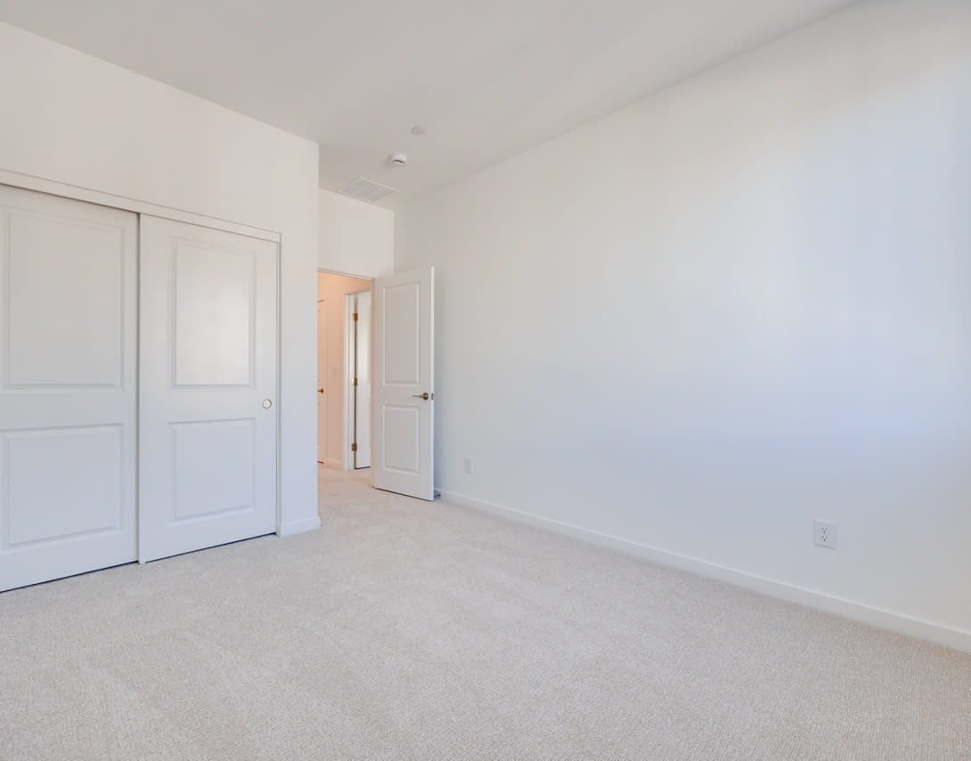 A spacious, minimalist room with white walls, sliding doors, and a carpeted floor.