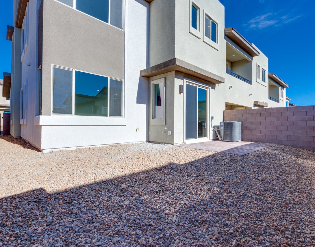 A modern, two-story residential building with a gravel driveway and a clear blue sky in the background.